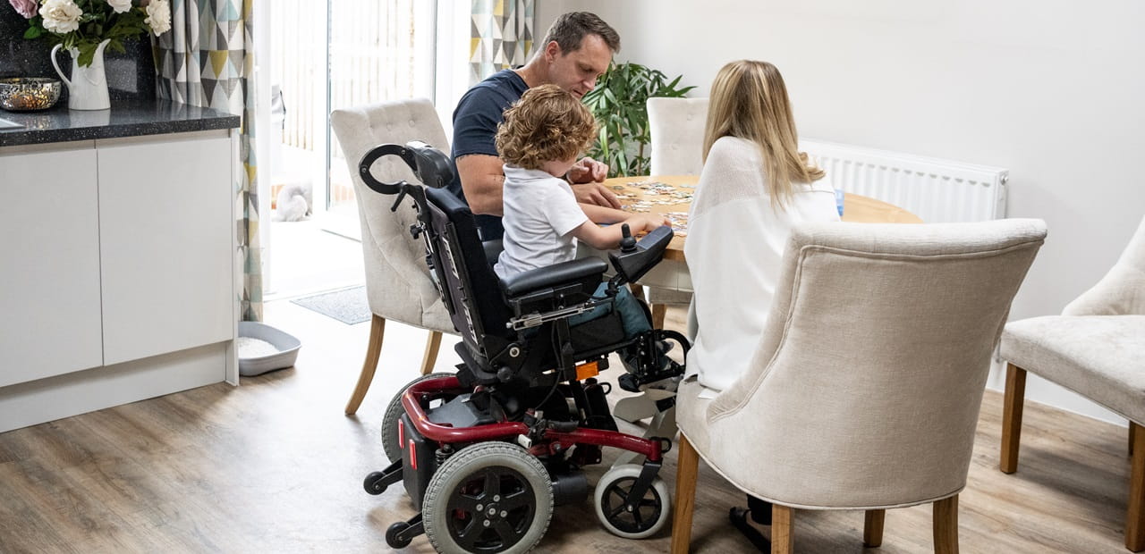 Boy in wheelchair playing a game with his parents.