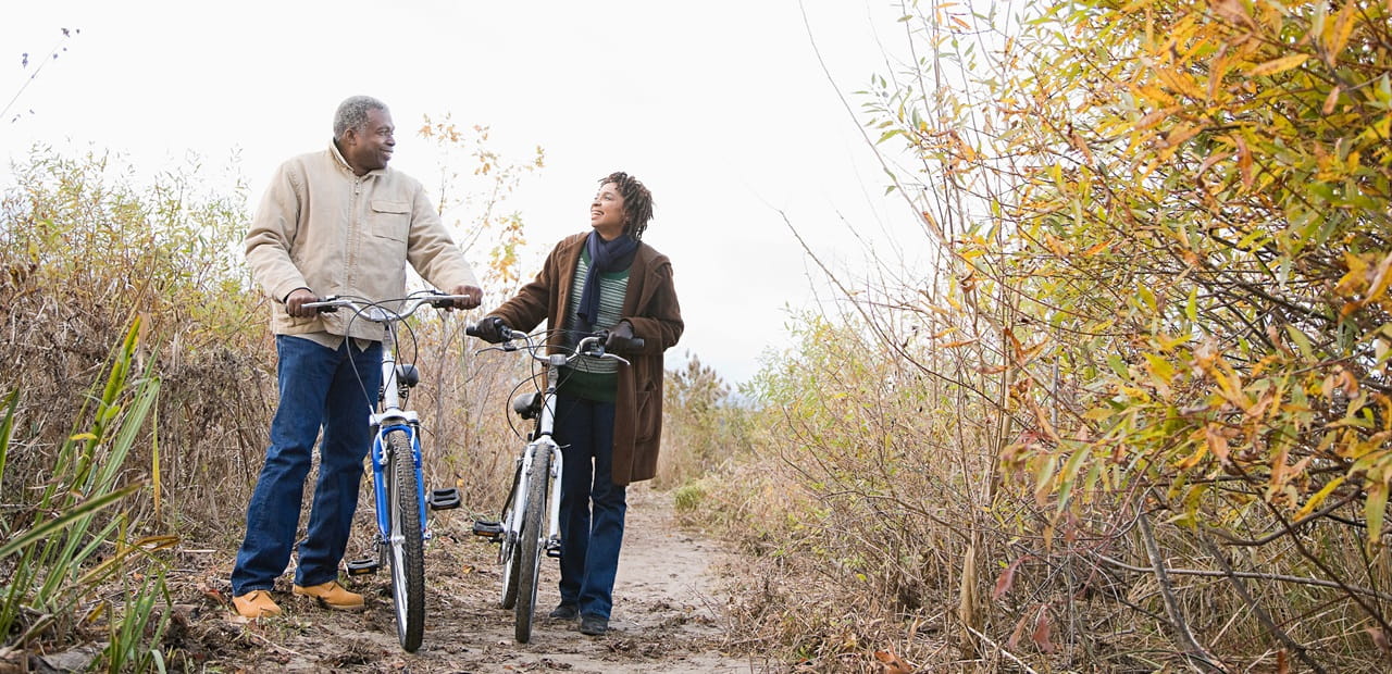 Mature couple pushing bicycles on a nature trail.