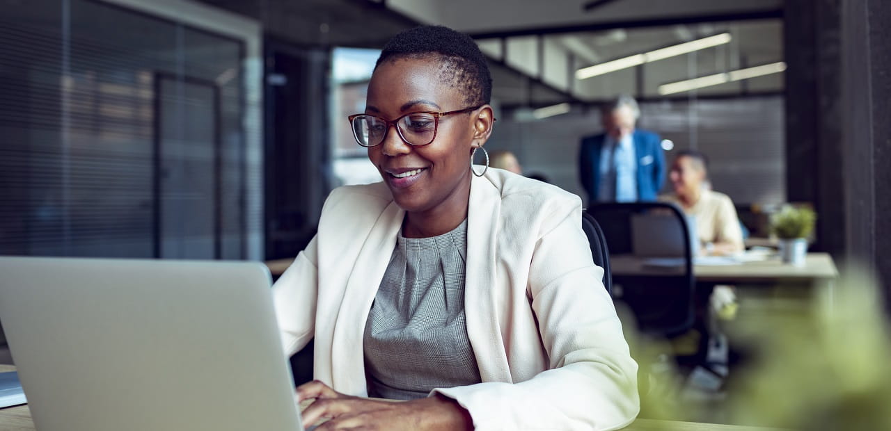 Woman sits at a desk in front of a laptop. 